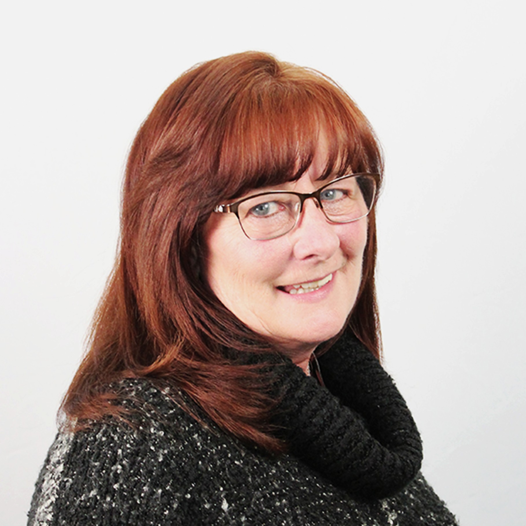 Red-haired woman wearing glasses and a black knitted scarf against a plain background.