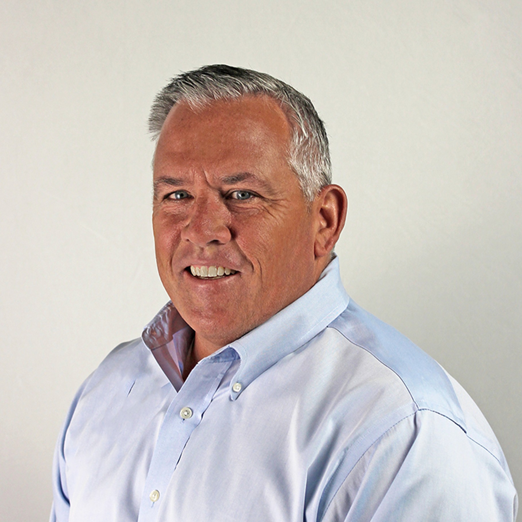 Professional Portrait of Man in Blue Shirt and Gray Hair A man in a light blue button-up shirt poses against a plain white background.