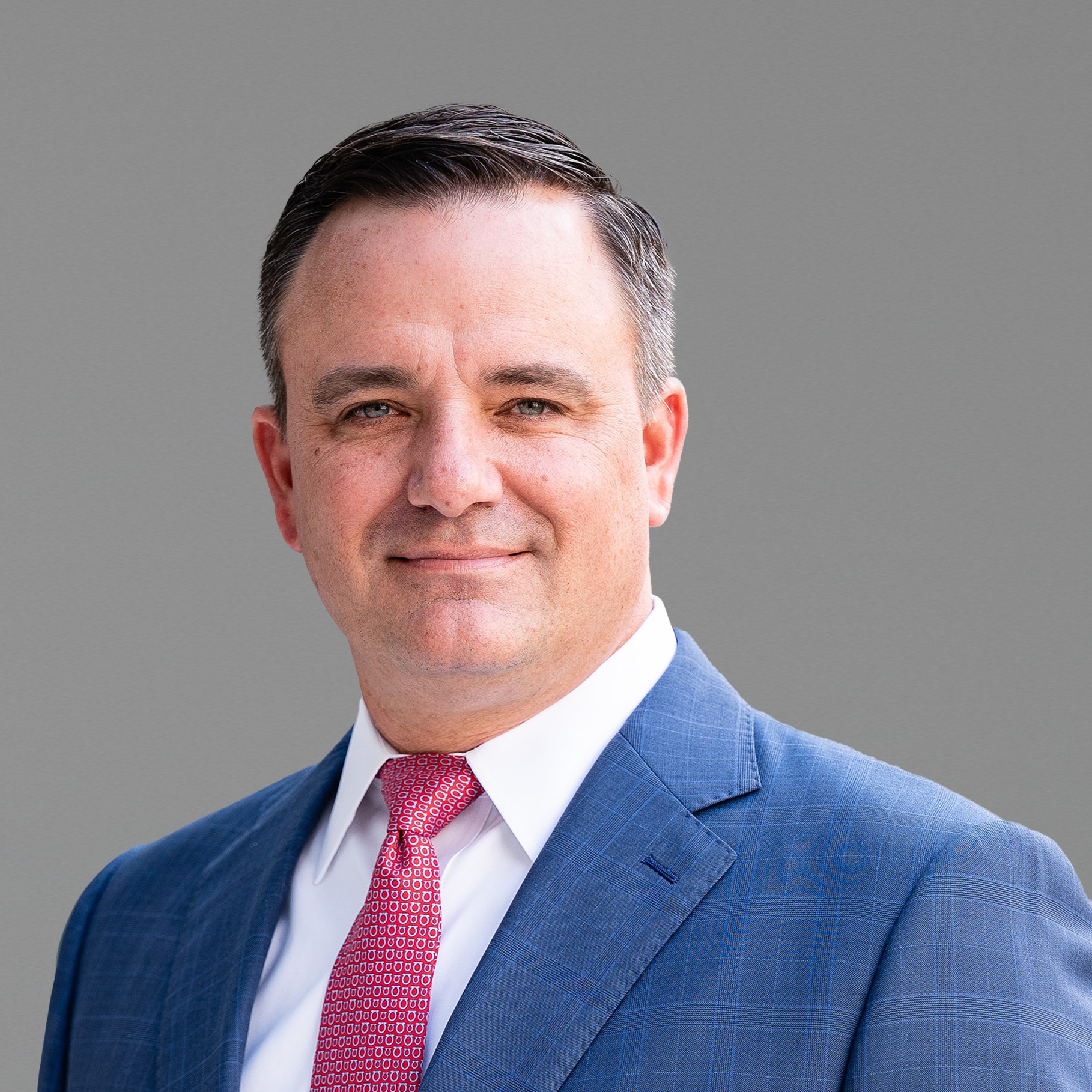 Professional man in blue suit and red tie on gray background Matt in blue suit and red tie against a plain gray background.