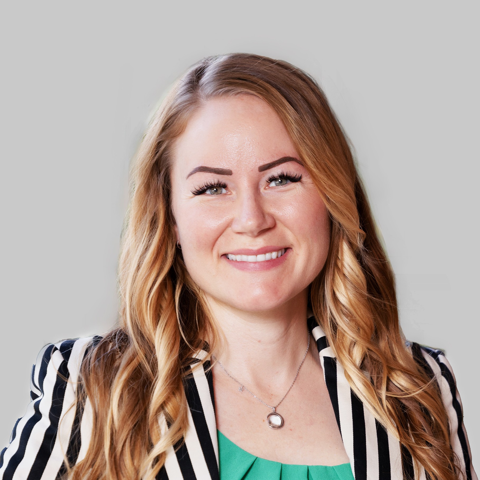 Woman with long wavy blonde hair wearing a black and white striped blazer and necklace.
