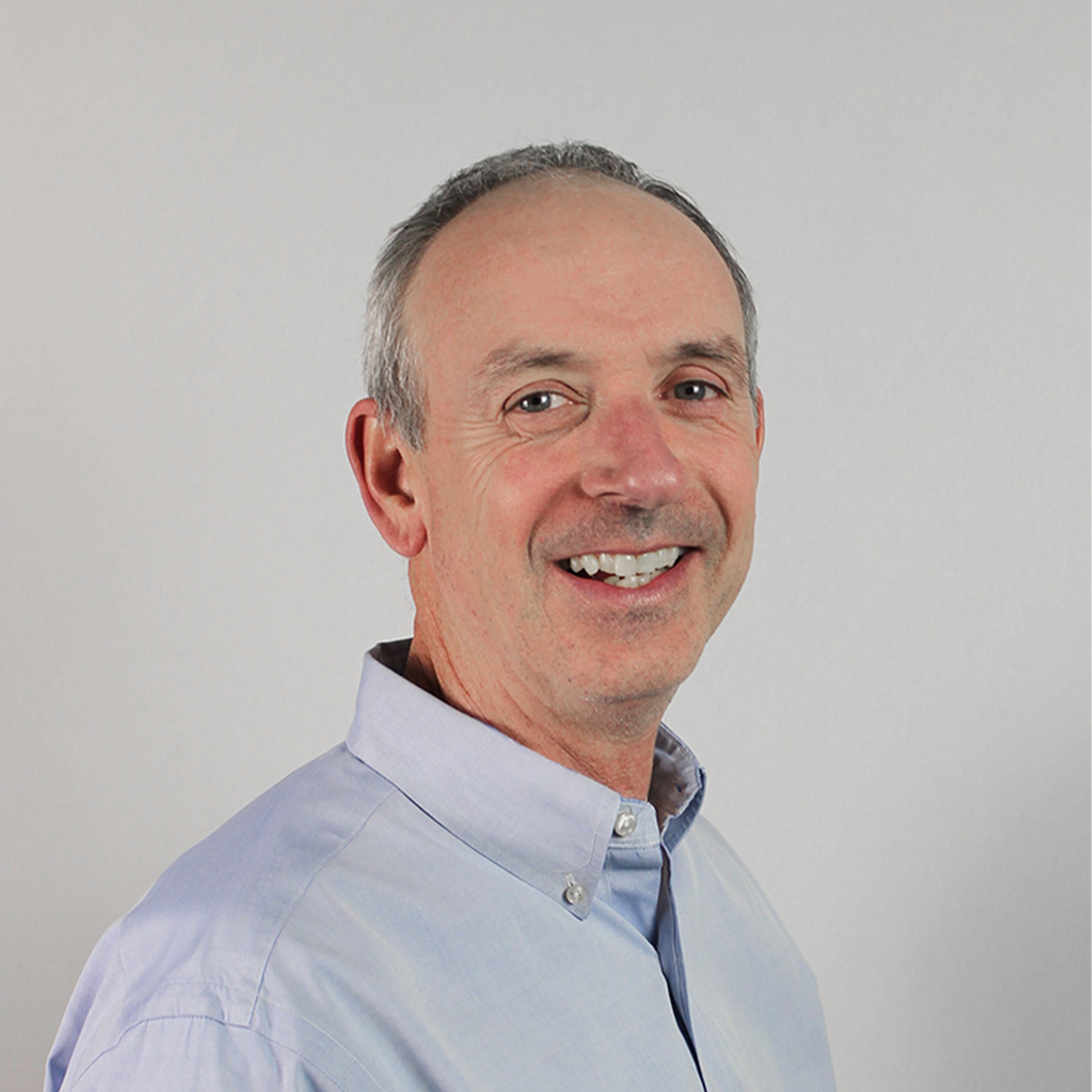Man in a light blue button-down shirt against a neutral background, facing slightly sideways.