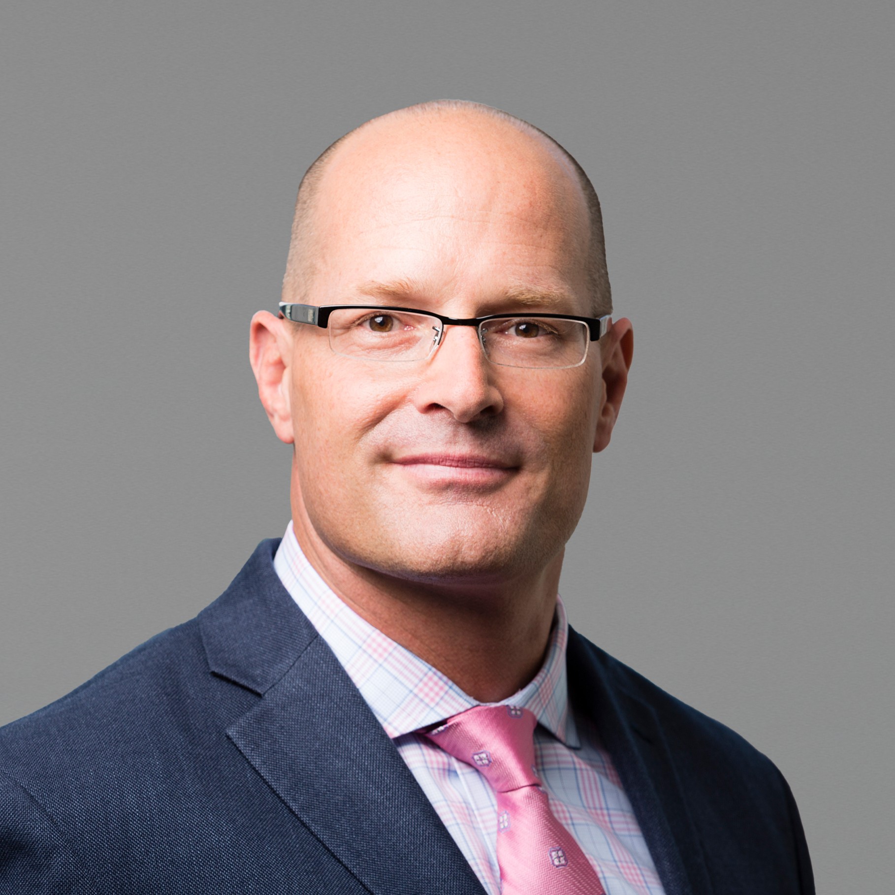 Professional businessman in suit with pink tie on gray background Russ in a dark suit, pink tie, and checkered shirt against a gray background.