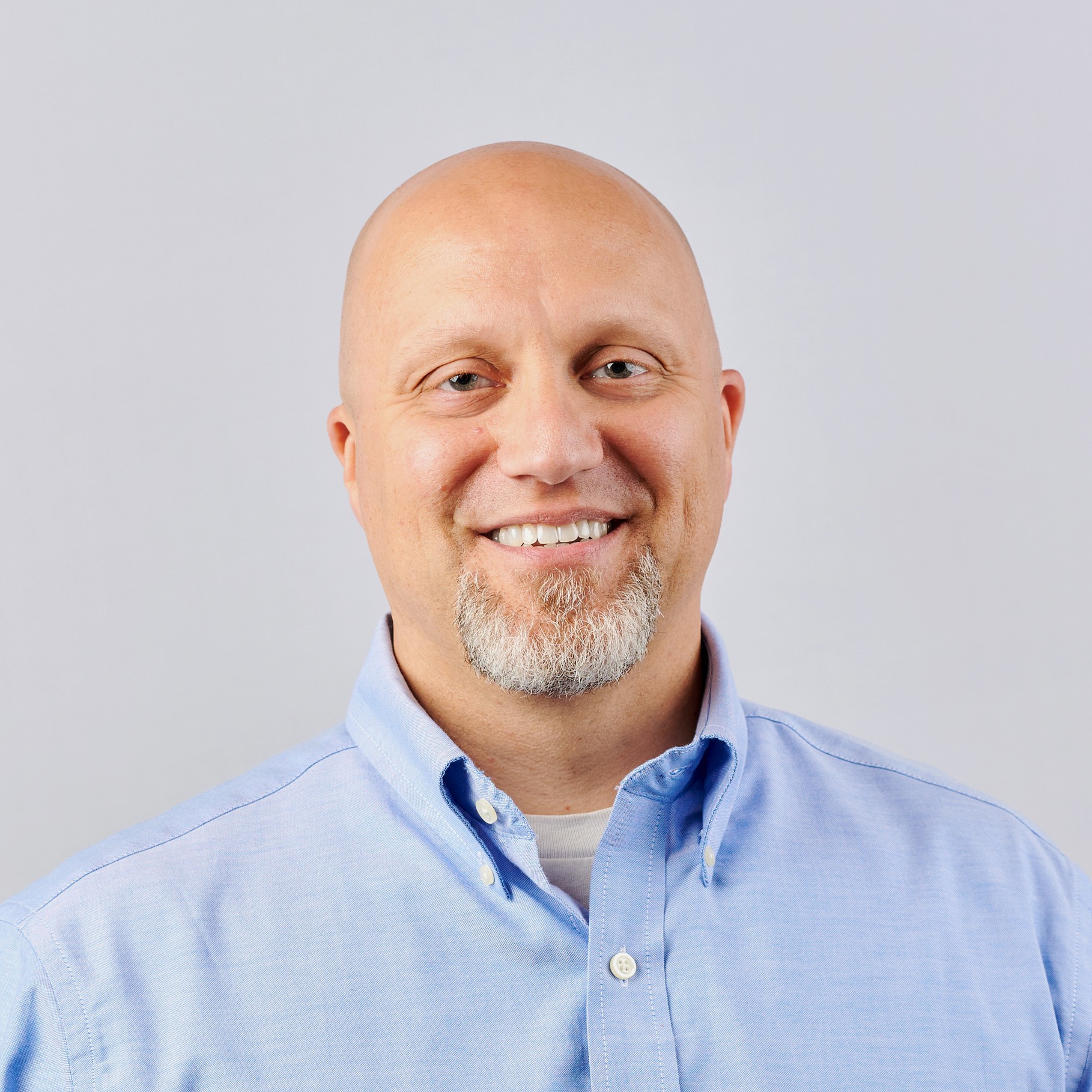 Man in Blue Shirt Against Plain Background A person wearing a light blue collared shirt against a plain gray background.