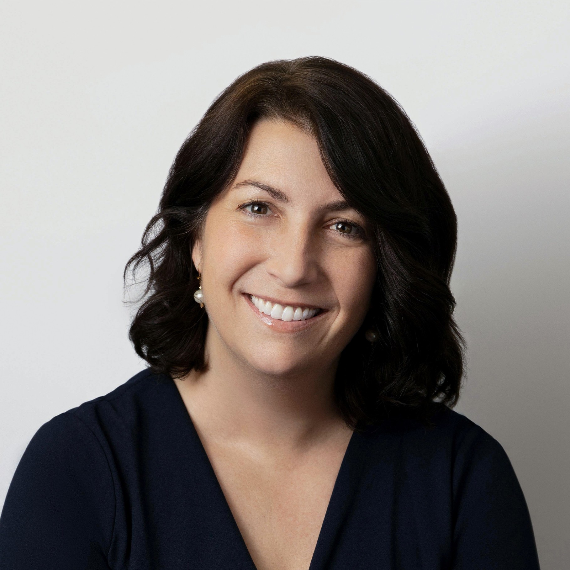 Woman with dark shoulder-length hair wearing a navy blue top against a plain white background.