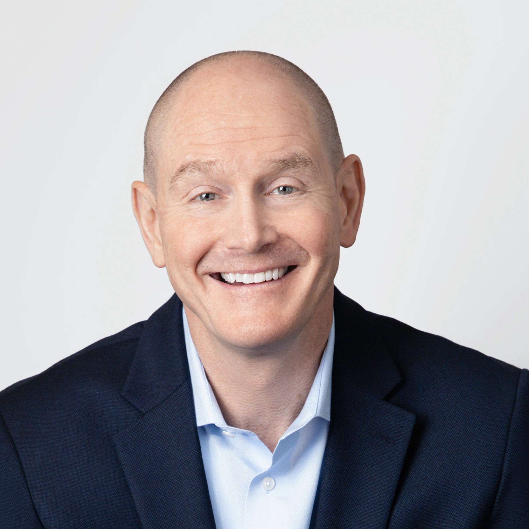 A man in a navy suit and light blue shirt against a plain white background.