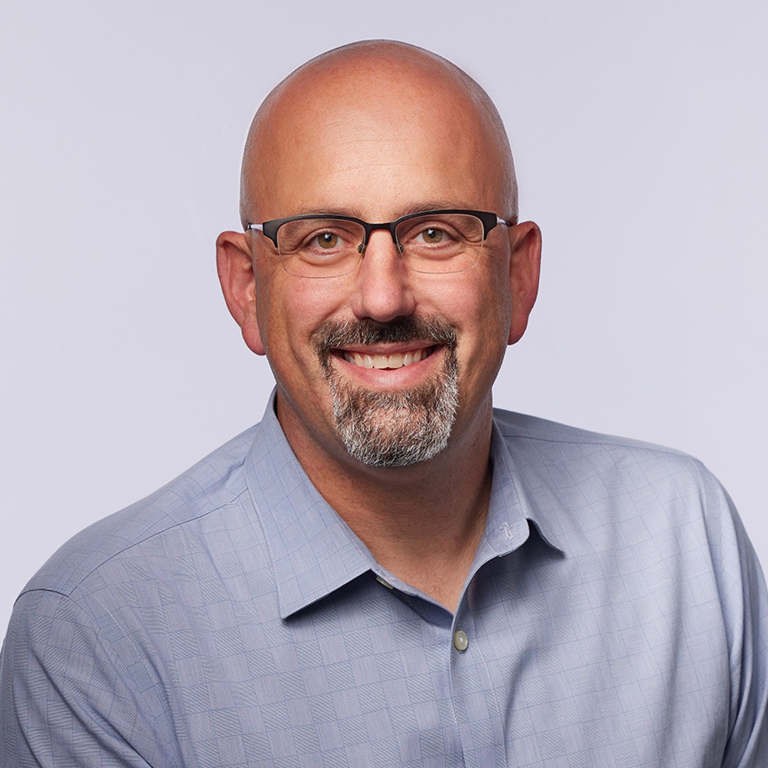 Man in Blue Checked Shirt Against Neutral Background A person in a light blue checkered shirt poses against a plain white background.