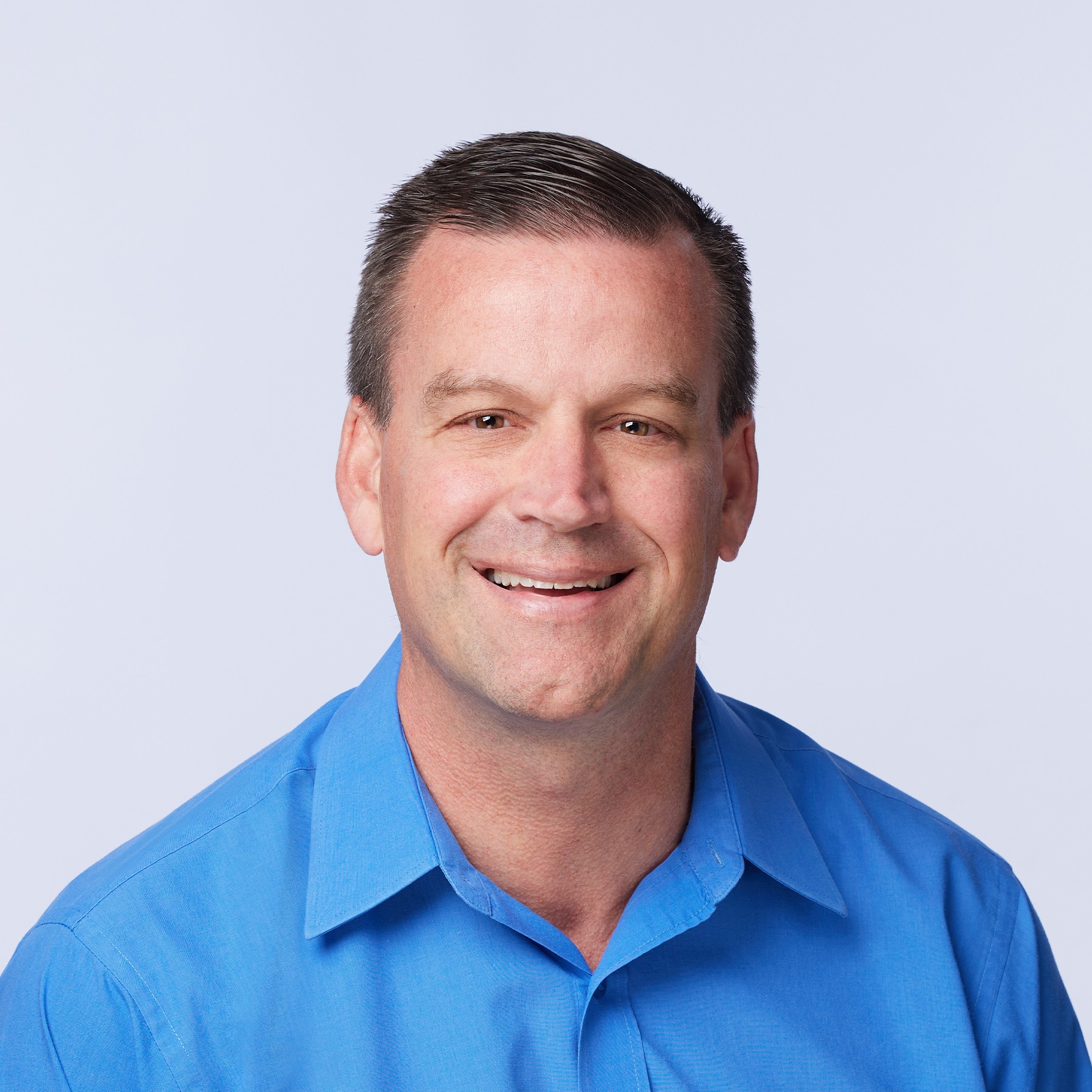 A person wearing a bright blue collared shirt against a light gray background.