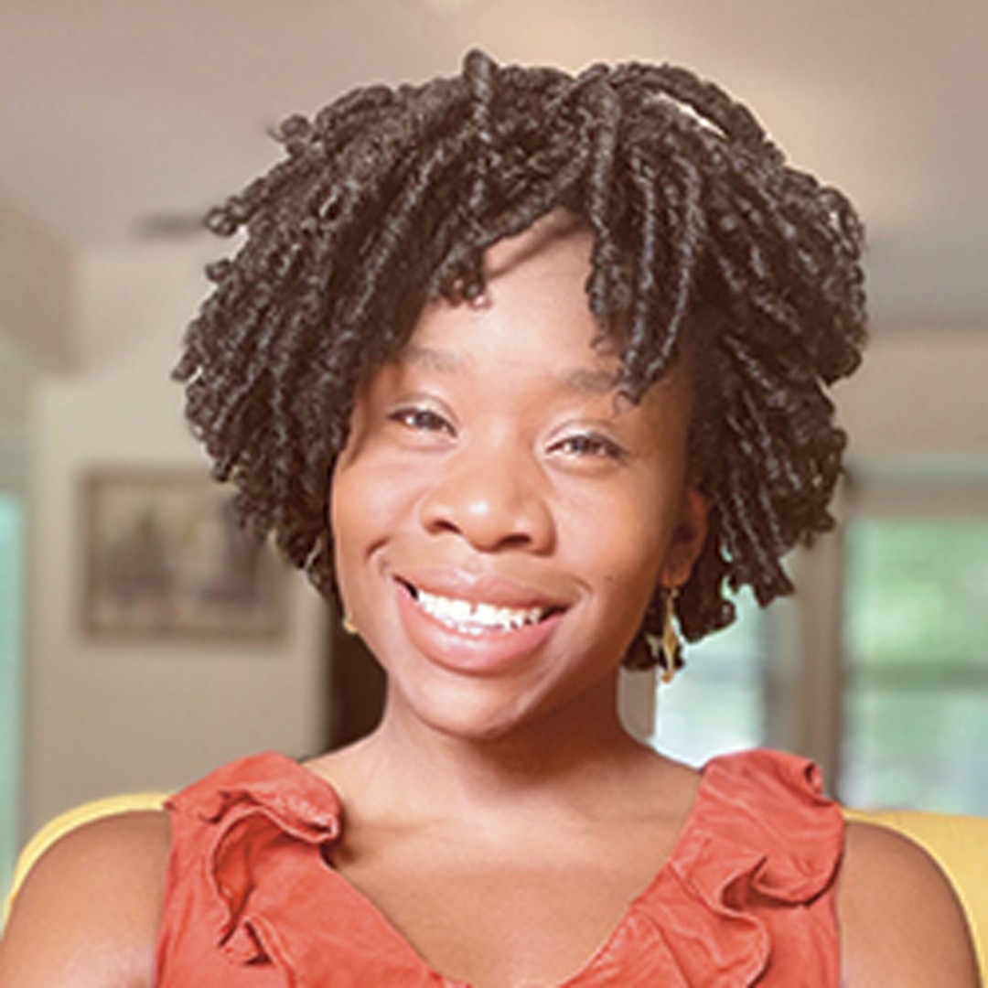 Stylish Twists Hairstyle with Elegant Coral Dress A person wearing a coral ruffled top has short, curly hair in a home setting with soft lighting.