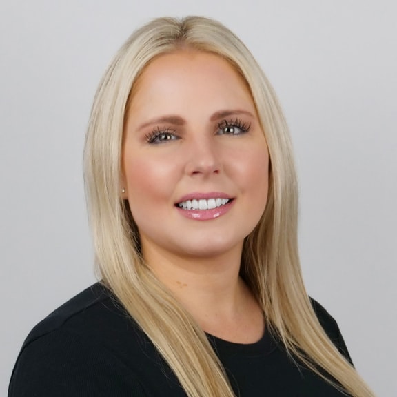 Blonde Woman with Long Hair Wearing Black Top on Gray Background Portrait of a smiling blonde woman with long hair wearing a black top against gray background.