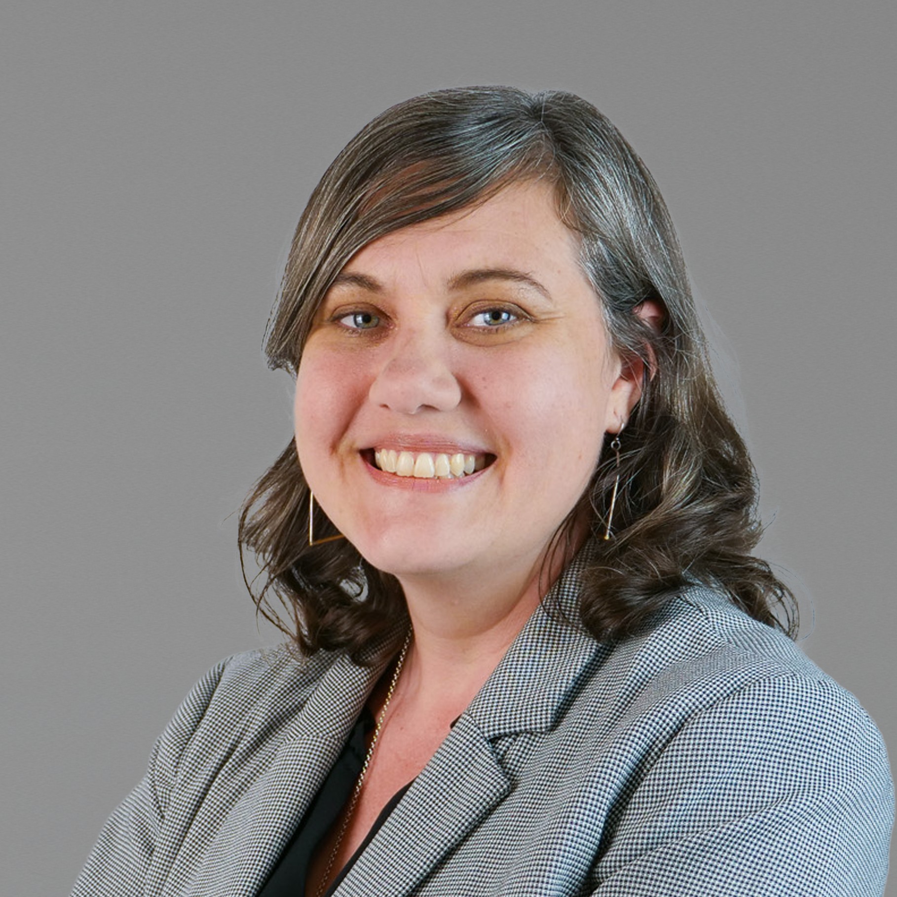 Jessica with gray hair wearing a checked blazer on a gray background.