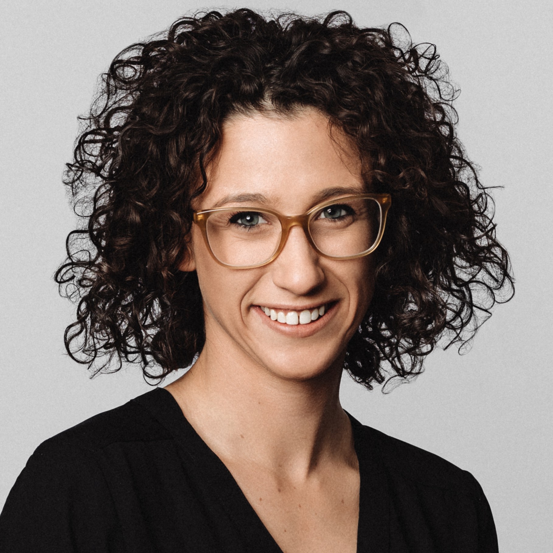 Curly Hair Woman Wearing Black Top with Glasses on Gray Background Woman with curly dark hair wearing a black top against a plain gray background.