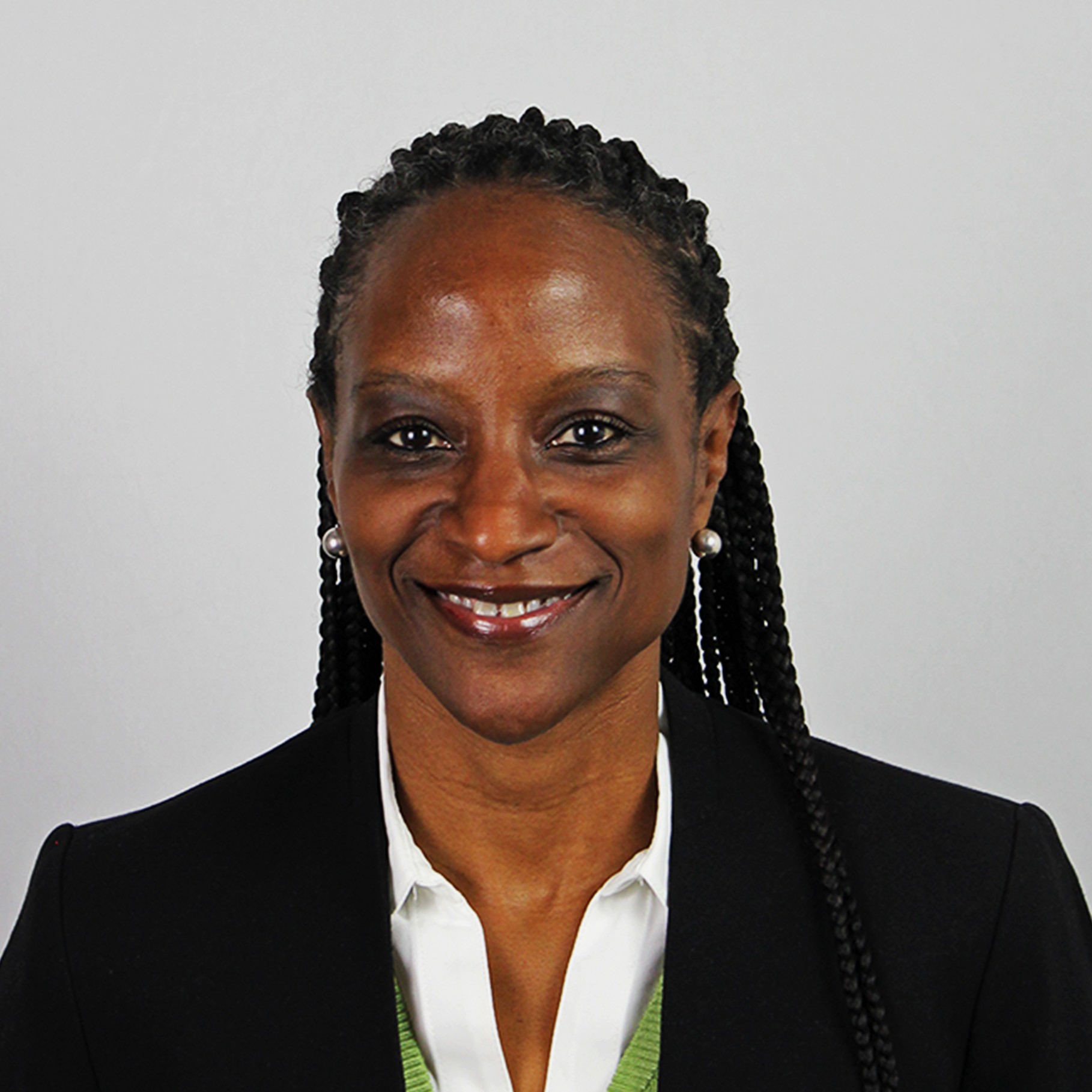 Professional woman with braided hair wearing a black blazer and white shirt against gray background.