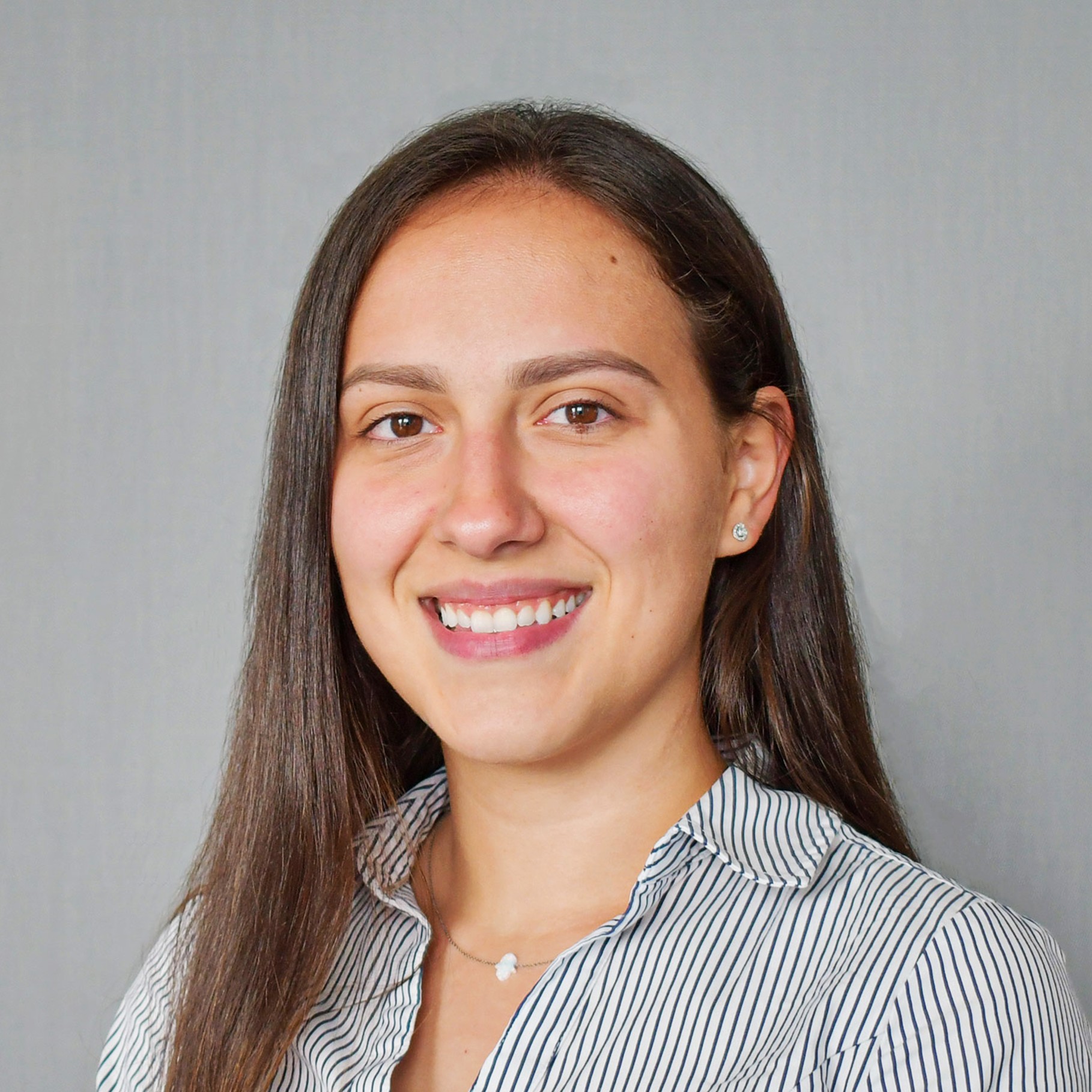Portrait of a woman with long brown hair wearing a striped shirt against a gray background.