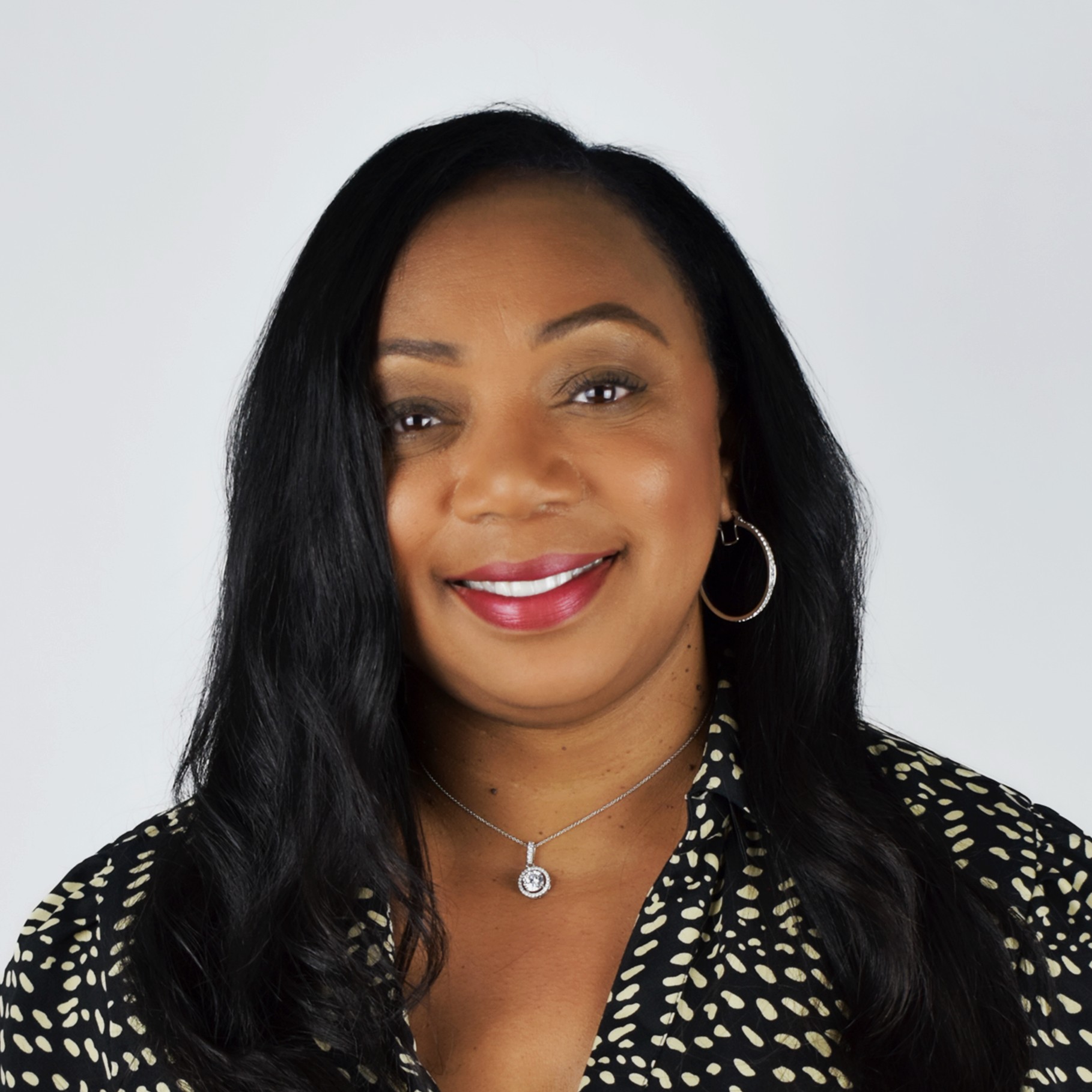 Professional woman with long black hair wearing a patterned blouse and silver jewelry.