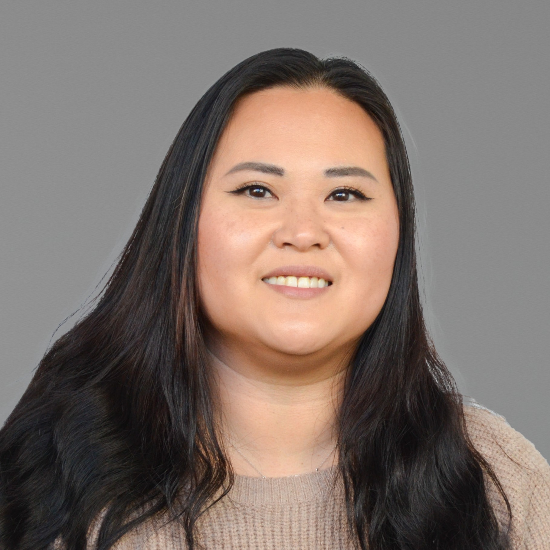 Sarah with long dark hair wearing a beige sweater against a gray background.