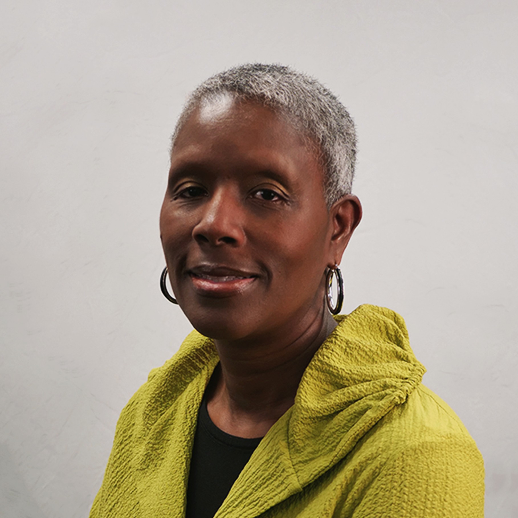 Portrait of a mature person with short gray hair wearing a textured yellow jacket.