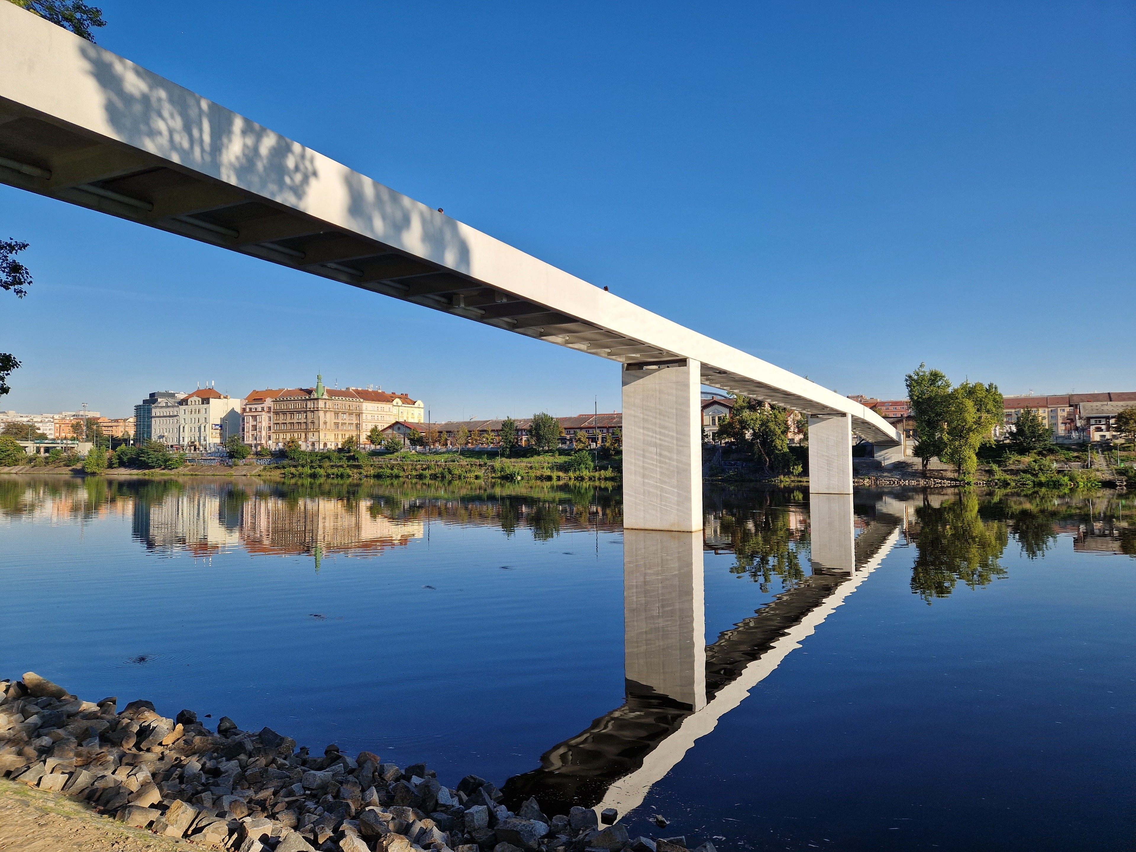Štvanice footbridge in Prague Modern pedestrian bridge over a river with trees and cityscape in the background.