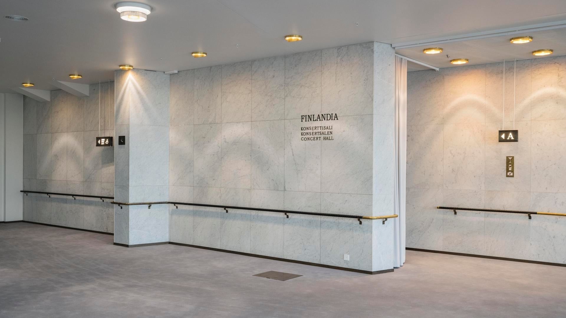 Interior of the Finlandia Concert Hall with marble walls, ceiling lights, and signs.
