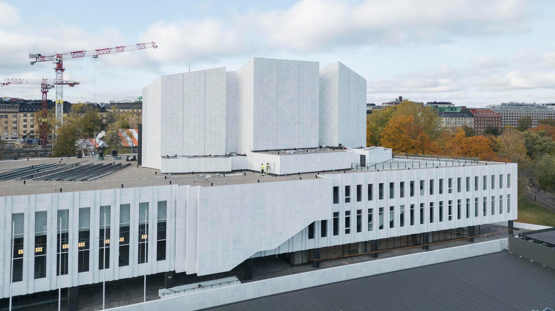 The basic renovation of the protected site took into account the value of the building and the preservation of cultural heritage. Modern white concrete building with angular design, surrounded by trees and urban landscape in Helsinki.