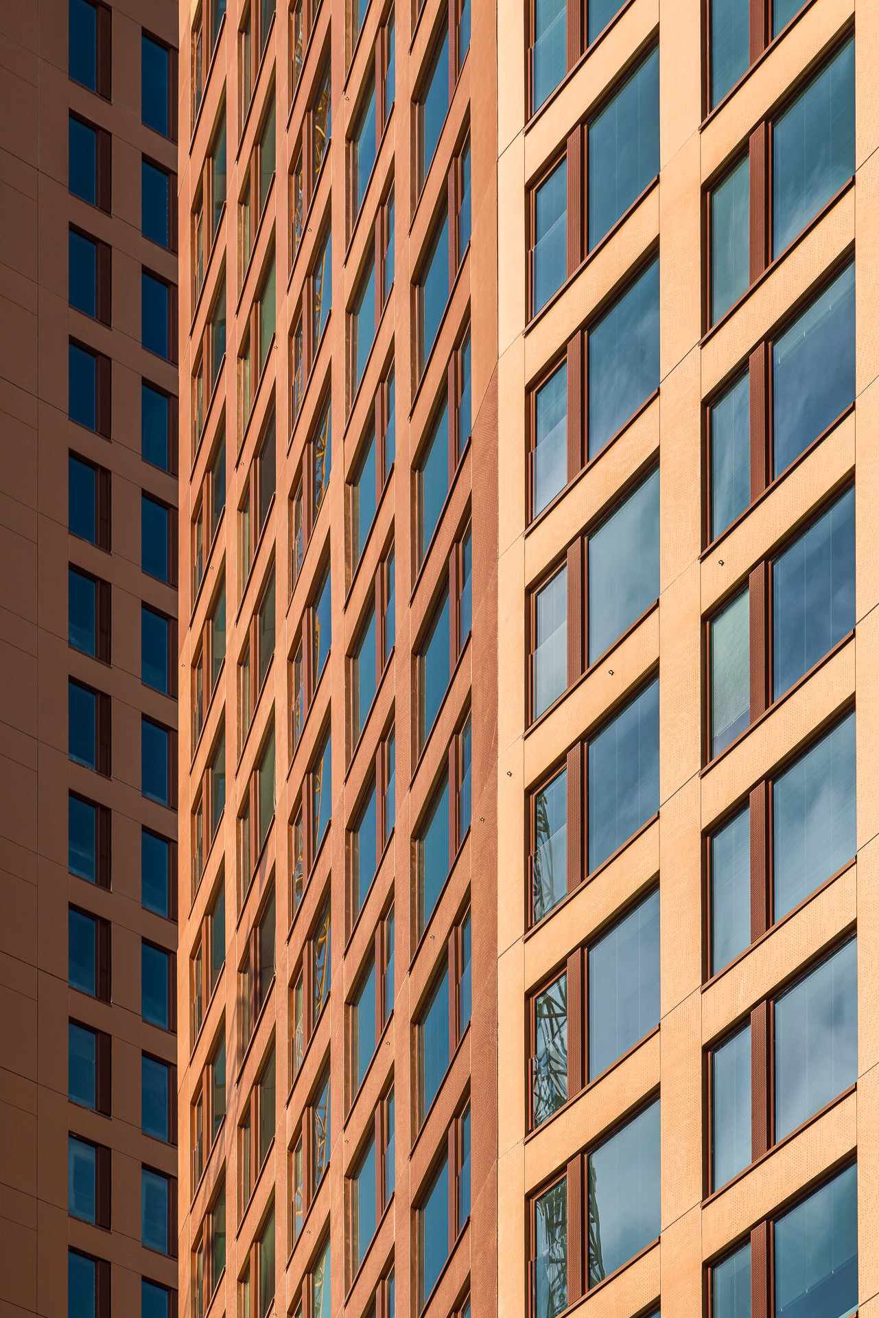 The striking facades of the tower houses are made of concrete with a metal-shimmering bronze shade, featuring graphic patterns. Close-up of the facades of bronze-glossy tower buildings with many windows.