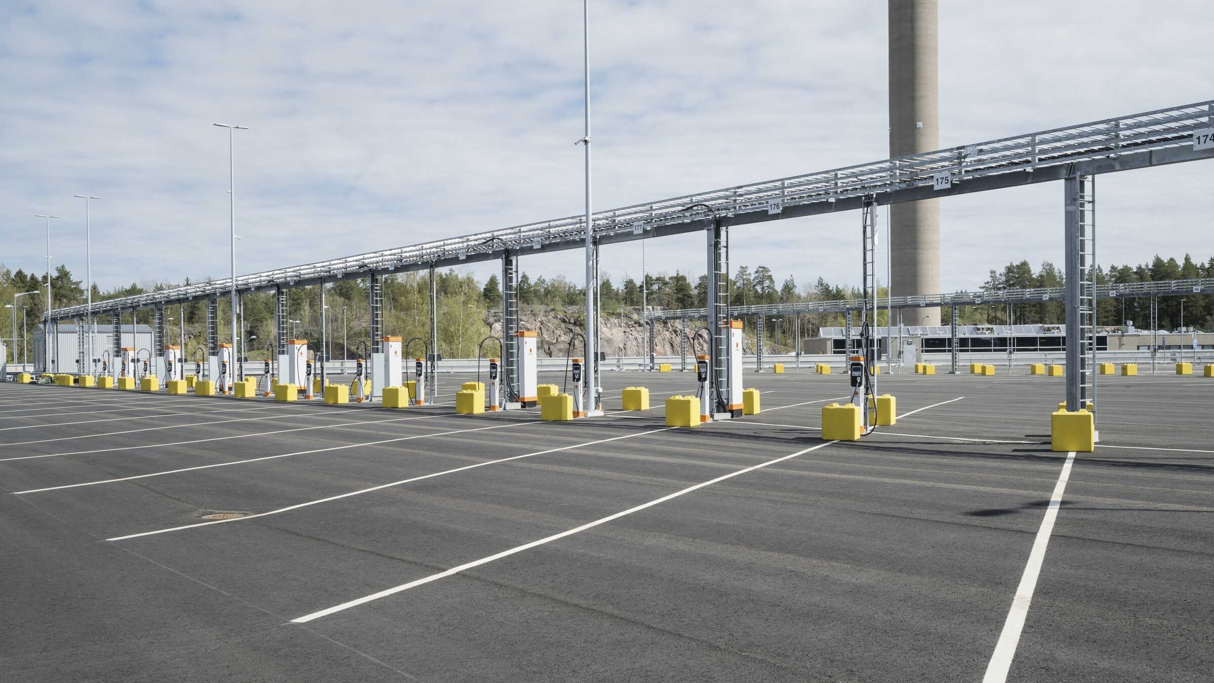 Empty parking lot with numerous charging points and a large industrial tower in the background.