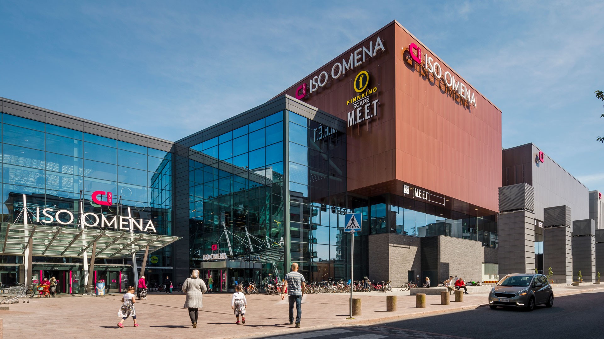 Modern shopping center Iso Omena in Finland with people walking and a car in front.