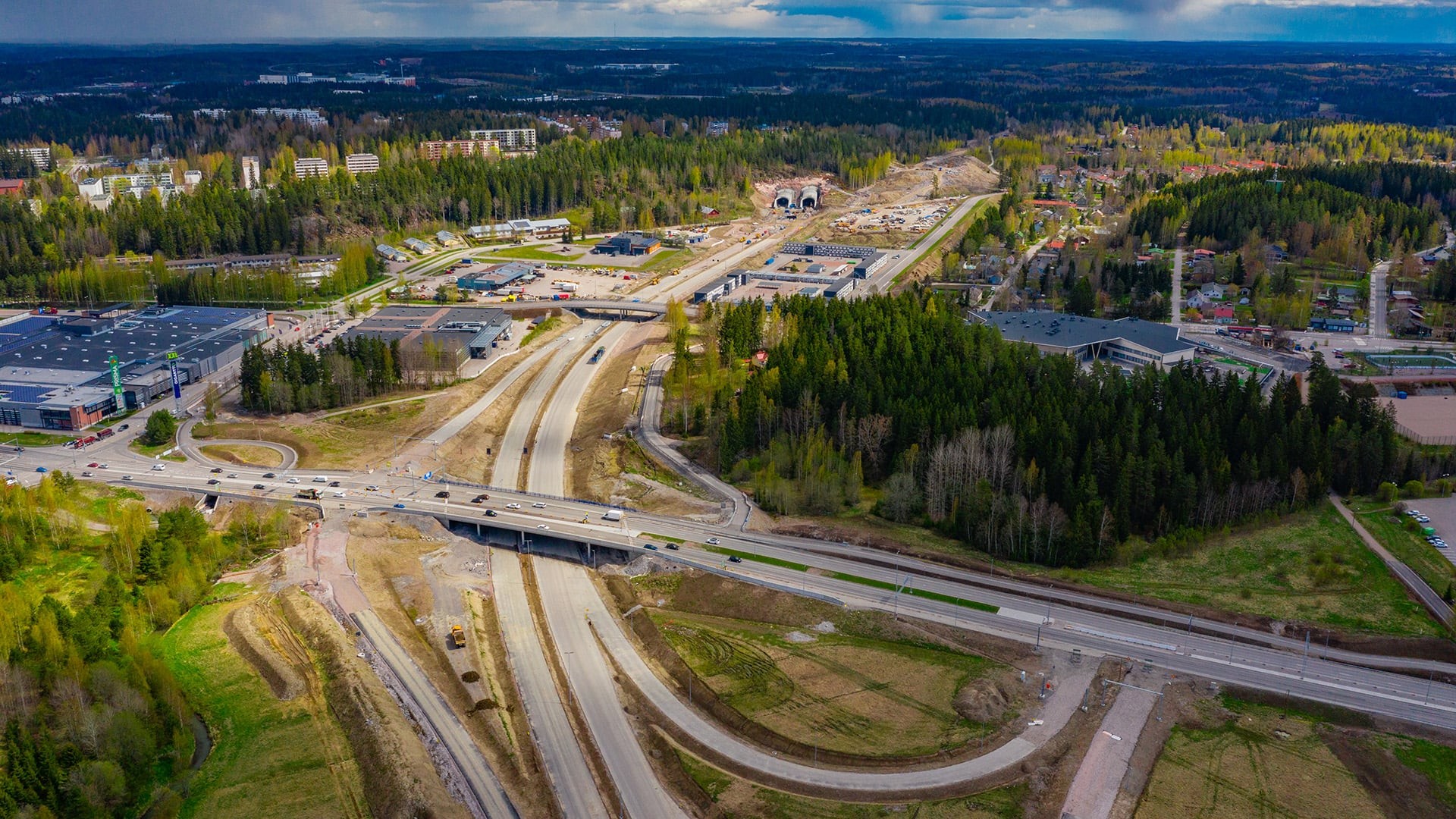 The new ring road in Lahti has added to Skanska’s already extensive experience on large-scale infrastructure projects. The enormous roadworks site includes, for example, more than a kilometre of tunnel structures, some of which are built under residential buildings. The project is applying for the BREEAM Infrastructure environmental certificate and is therefore aiming at minimising its carbon footprint, protecting groundwater, and preserving the surrounding biodiversity. Aerial view of highway construction surrounded by lush forest and urban development.