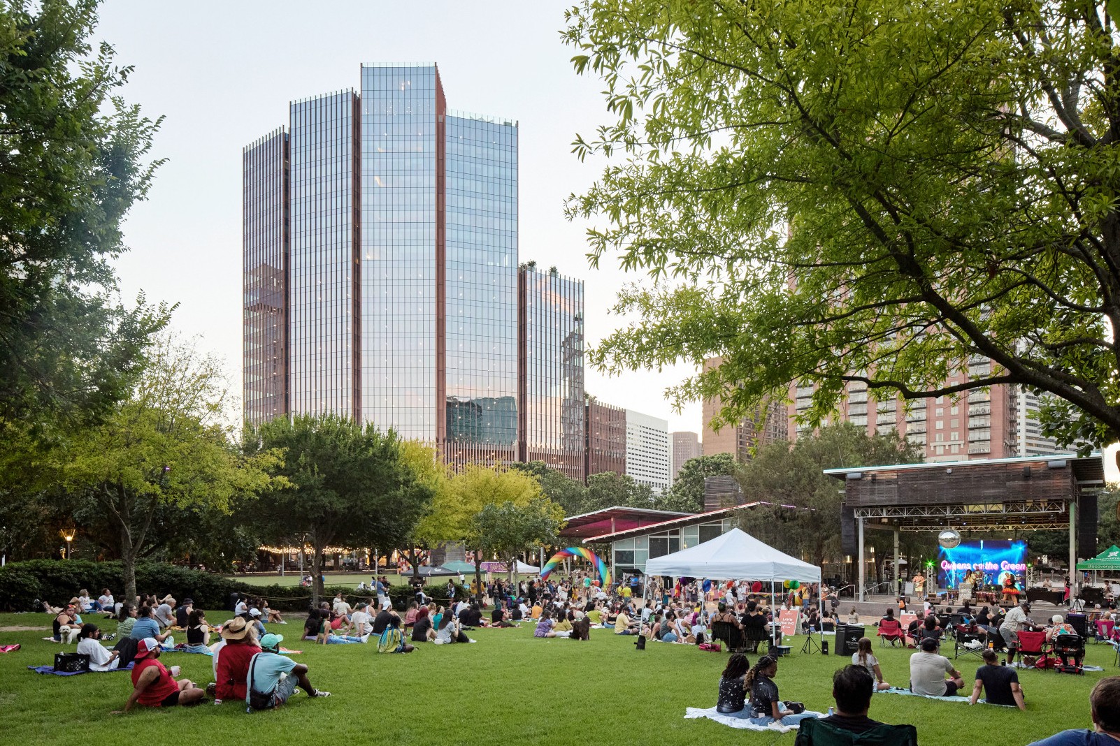 People gathered on a grassy park lawn near tall glass buildings during a community event.