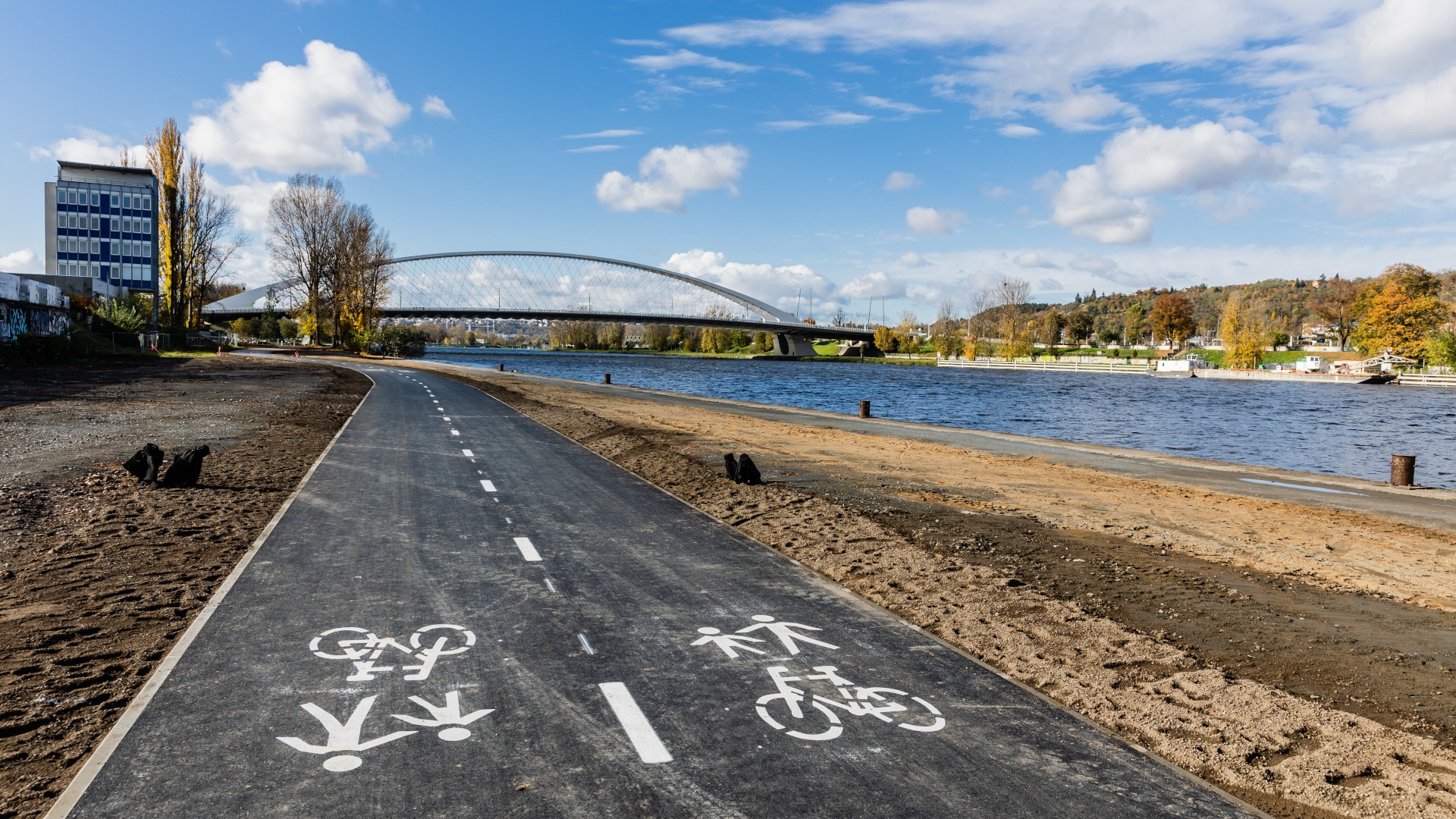 Riverfront bike path with pedestrian and cyclist lanes under a blue sky and bridge.