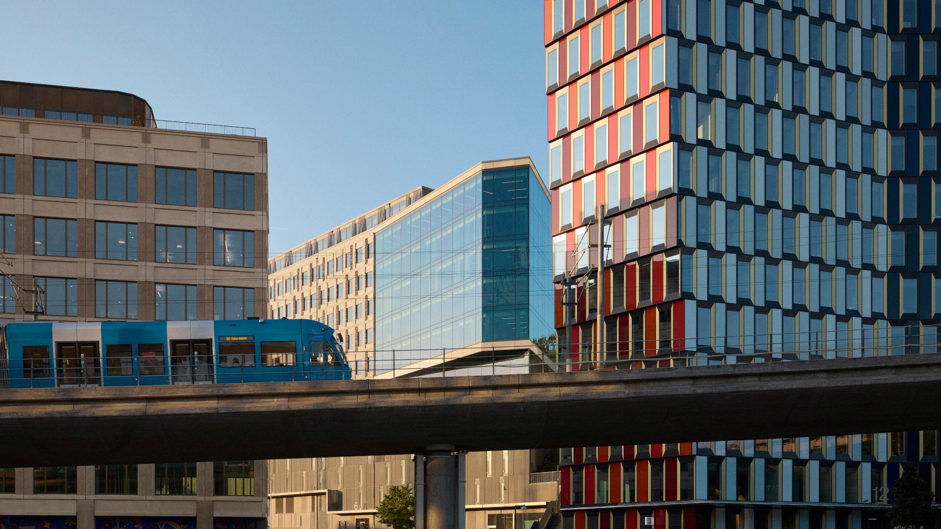 Modern cityscape with a blue tram passing on an elevated track between glass buildings.