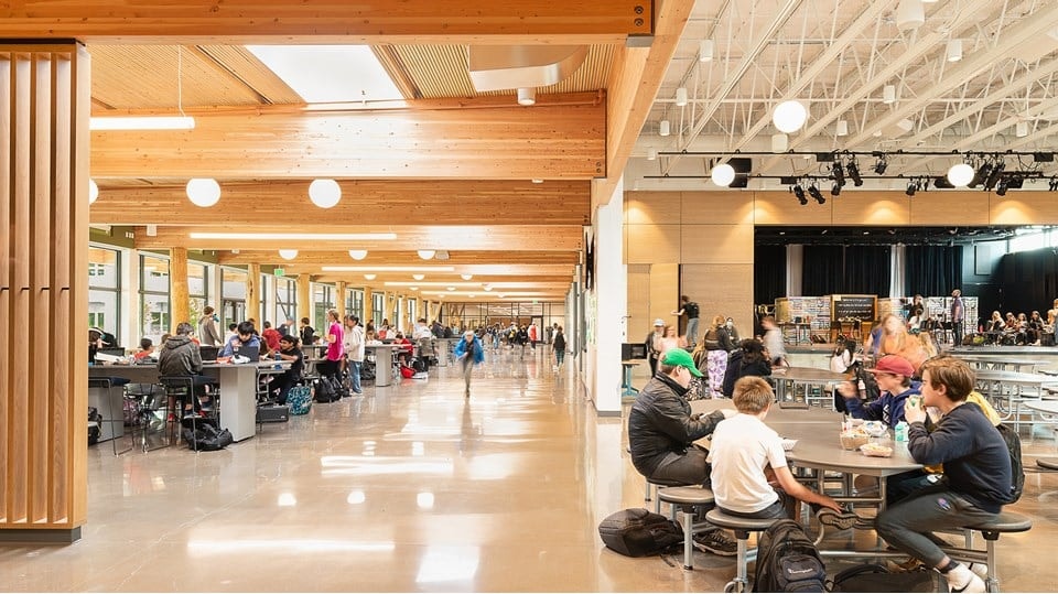 Spacious modern school cafeteria with students eating and socializing at tables.