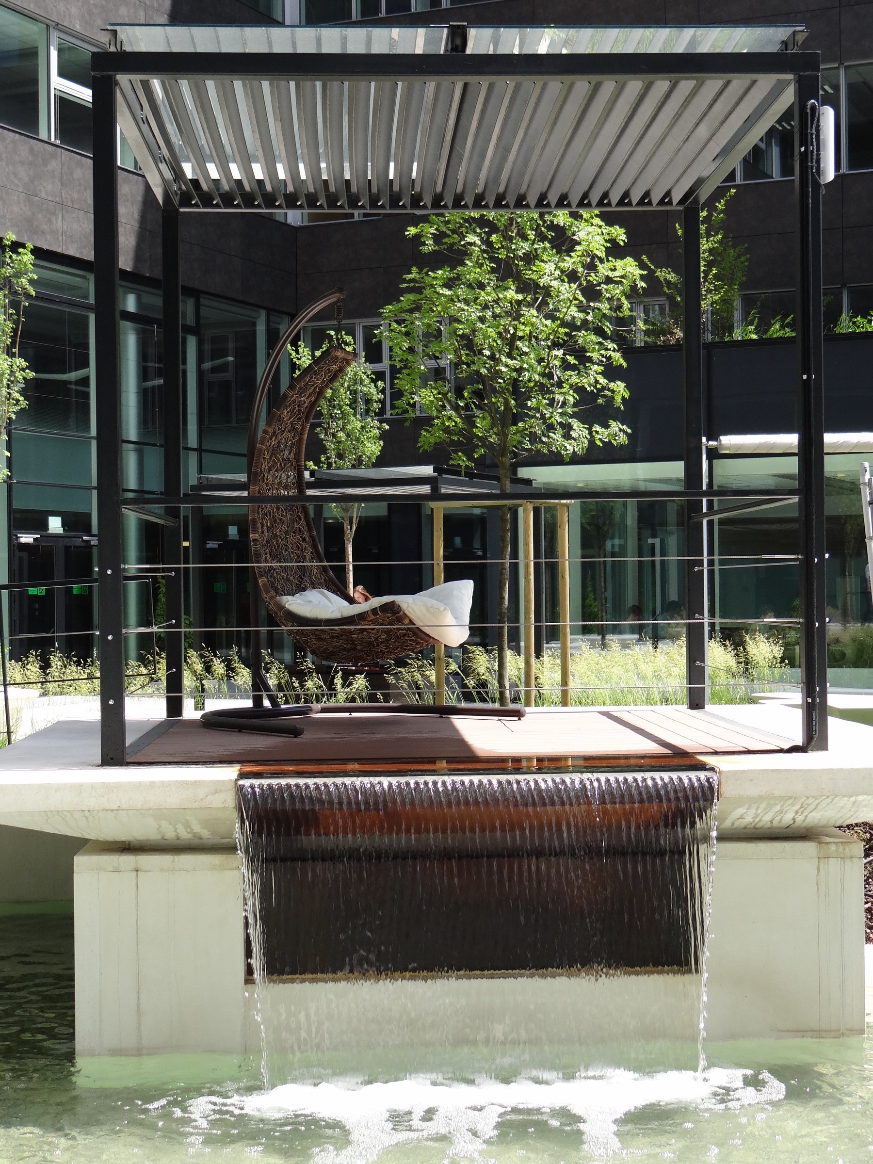 Green House Waterfall Modern outdoor lounge with a hanging chair and waterfall feature in a contemporary courtyard.
