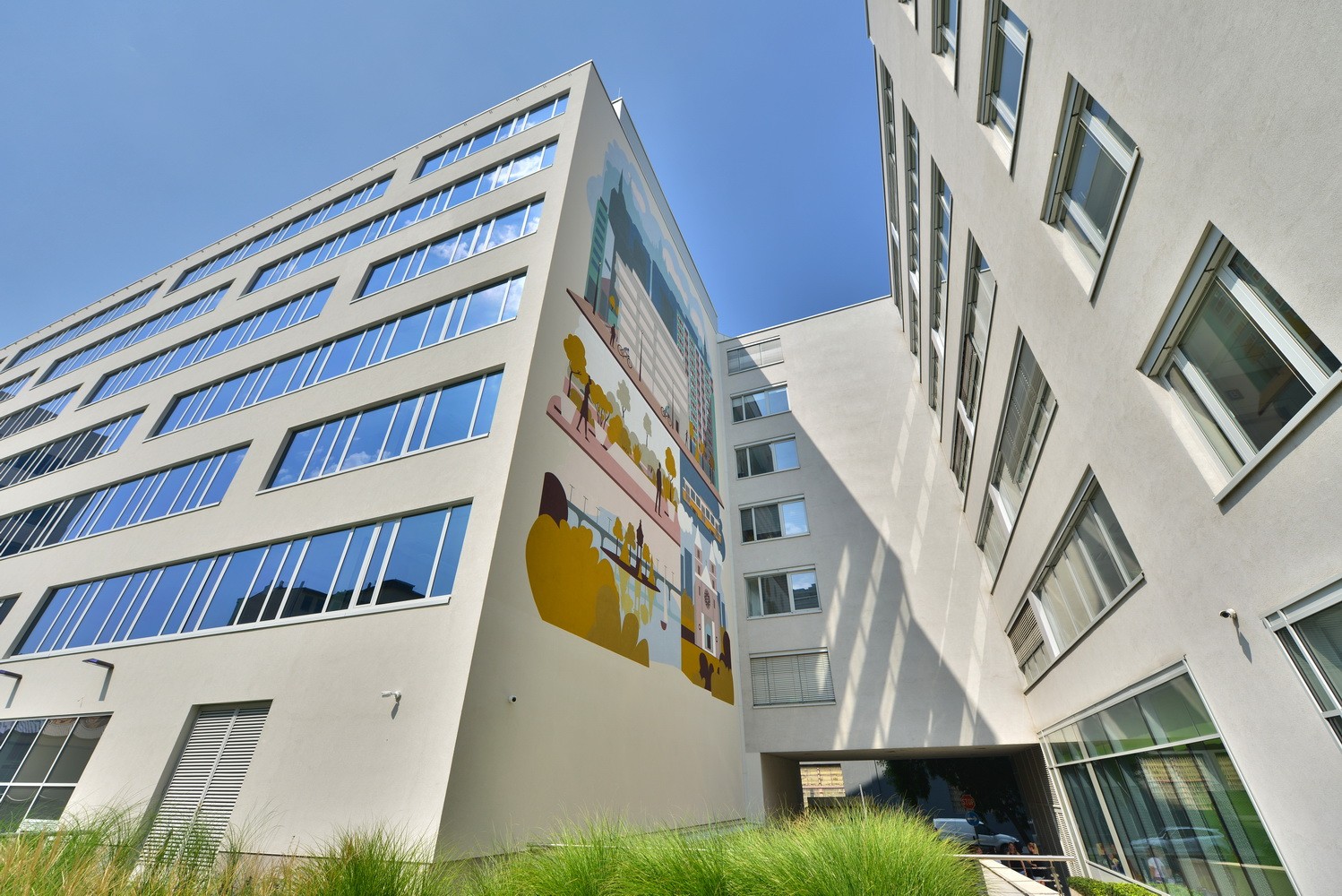 Modern building exterior with vibrant mural, featuring people and urban scenes under clear skies.