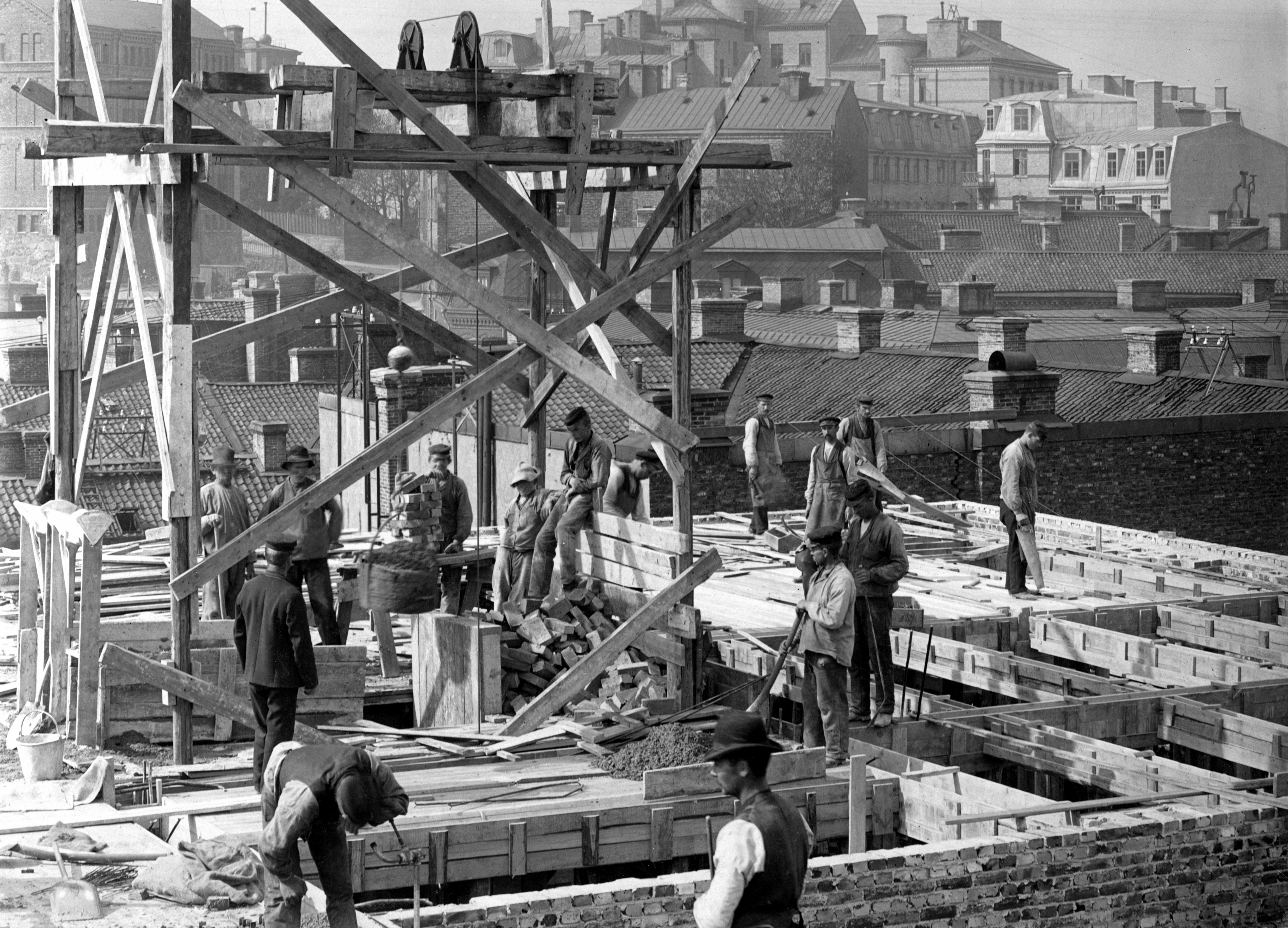 Construction workers building a structure with scaffolding in a busy urban area, circa early 1900s.