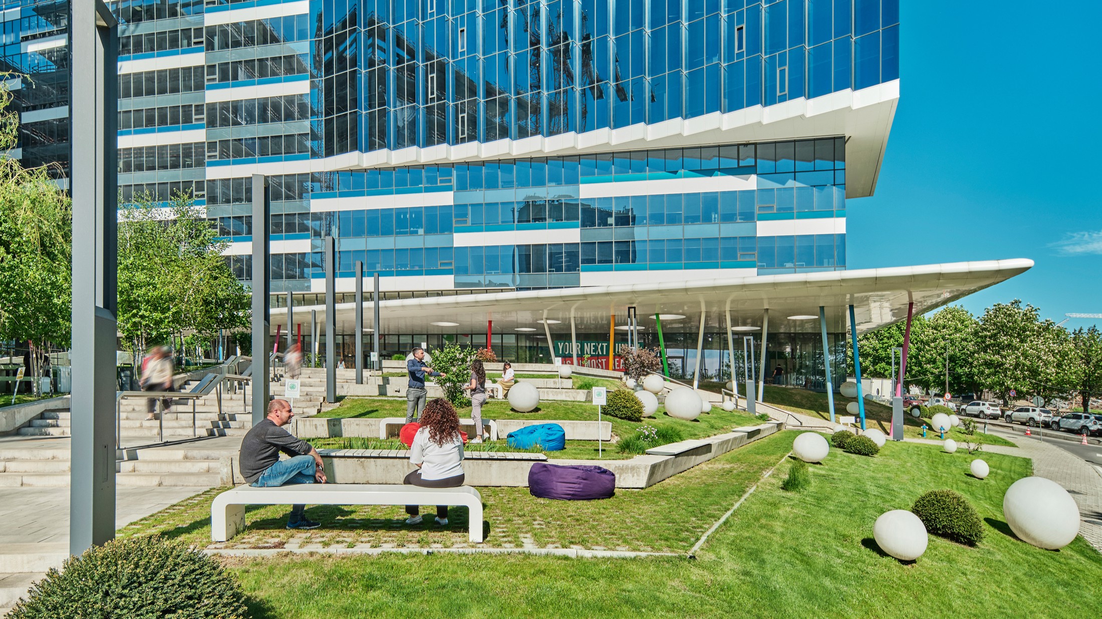 Equilibrium green area Modern office building with landscaped outdoor seating area featuring people enjoying the sunshine.