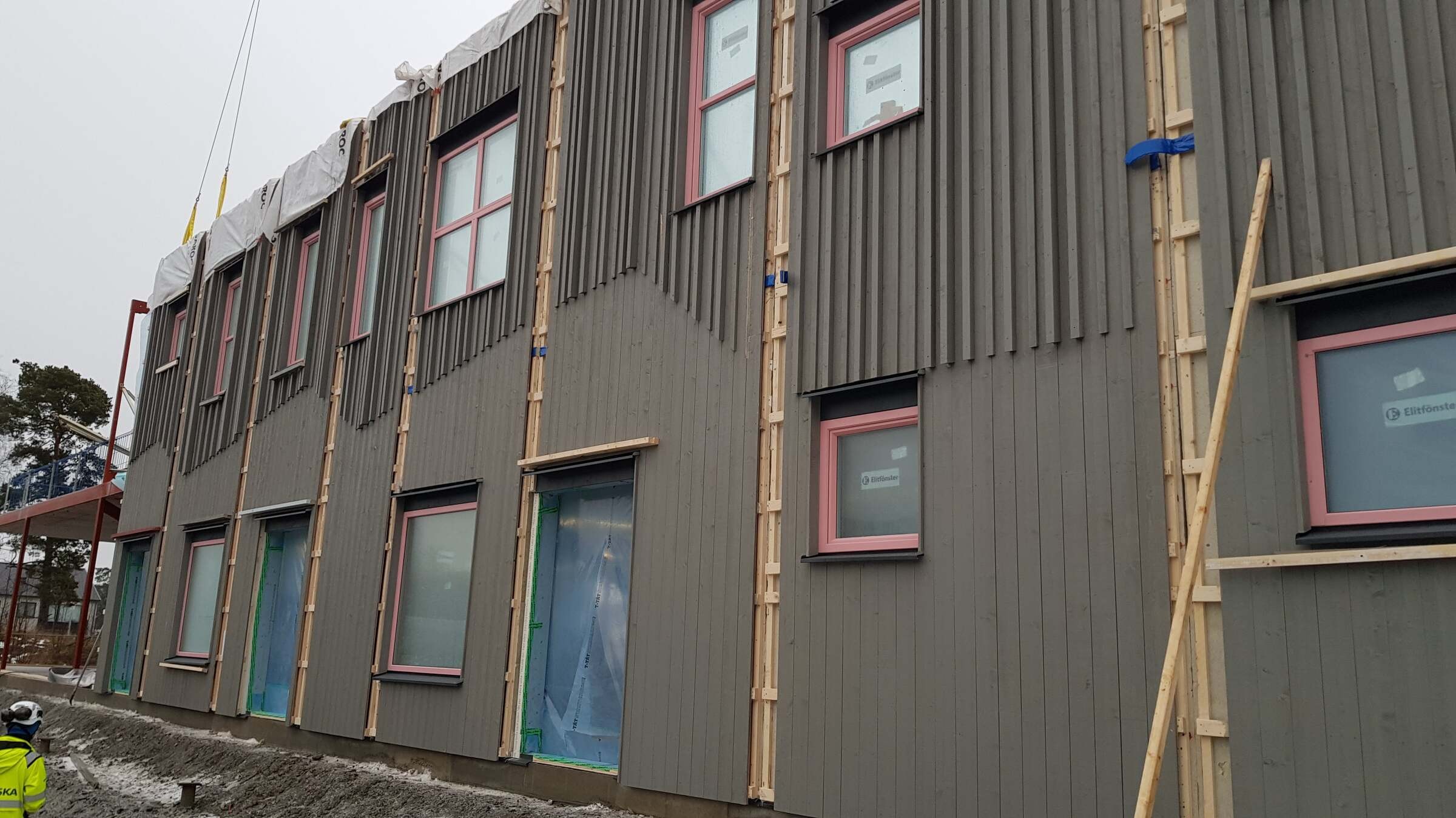 Construction site with partially completed building featuring vertical wood siding and windows.