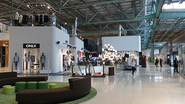 Modern shopping mall interior with clothing stores, stylish seating, and bright lighting fixtures.