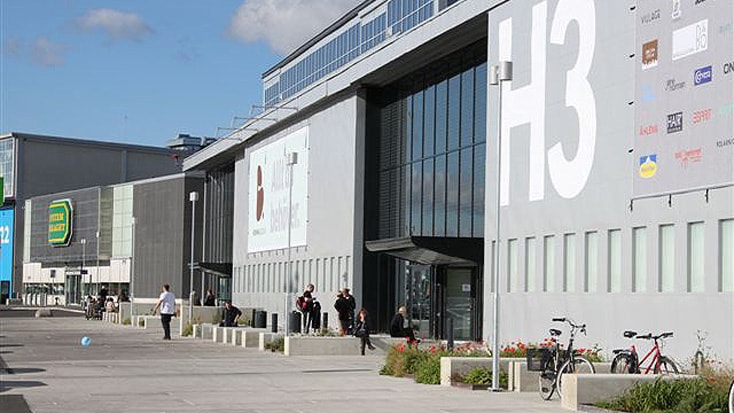 Modern industrial building labeled H3 with people outside and bicycles parked nearby.