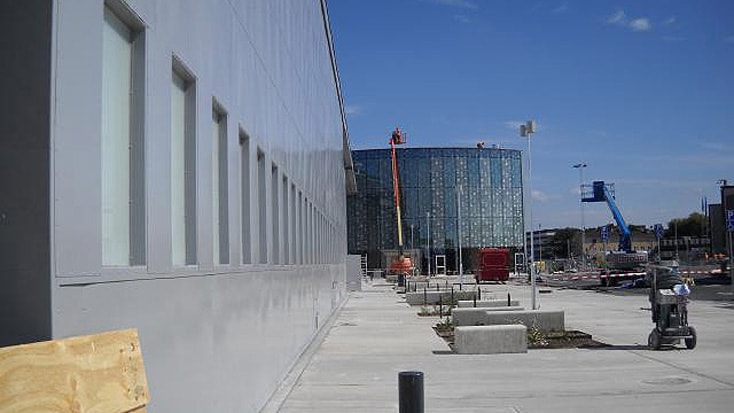Moderne Baustelle mit Kränen und Glasfassade unter klarem blauem Himmel.