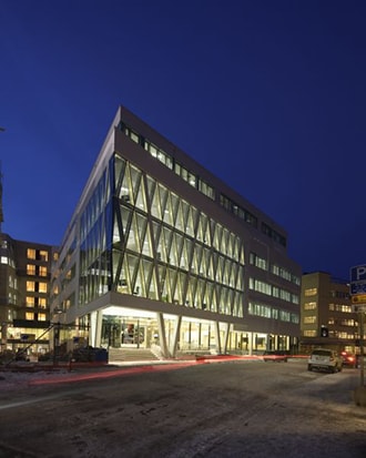 Modern glass-fronted office building illuminated at night in an urban winter setting.