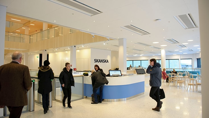 Modern office lobby with Skanska logo, people interacting at reception, and seating area in background.