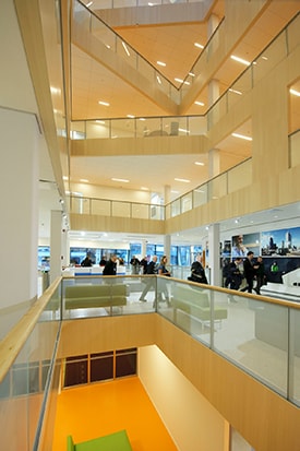 Modern multi-story atrium with glass railings, light wood accents, and people walking.