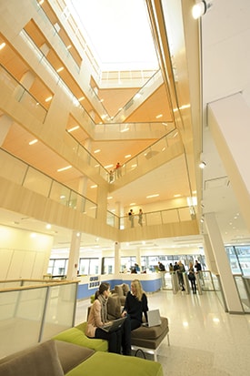 Modern atrium with multiple floors, glass railings, and people conversing on seating areas.