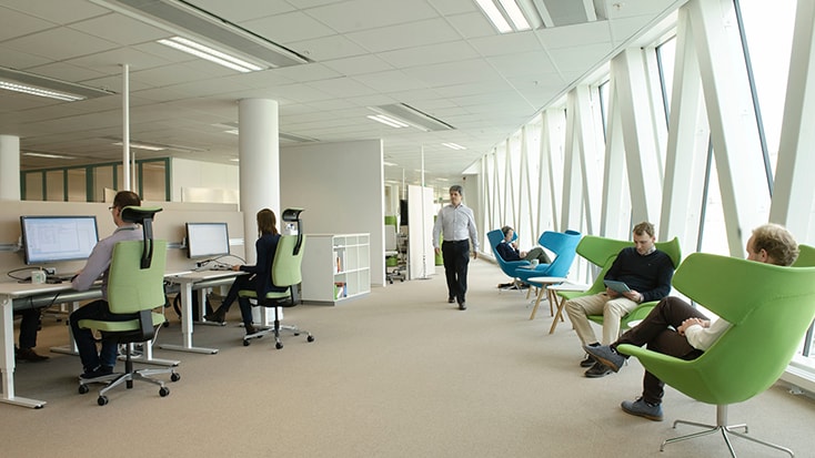 Modern open-plan office with people working at desks and relaxing in vibrant lounge chairs.