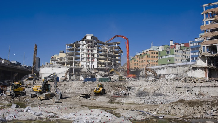 Construction site with heavy machinery demolishing a large, partially collapsed building.