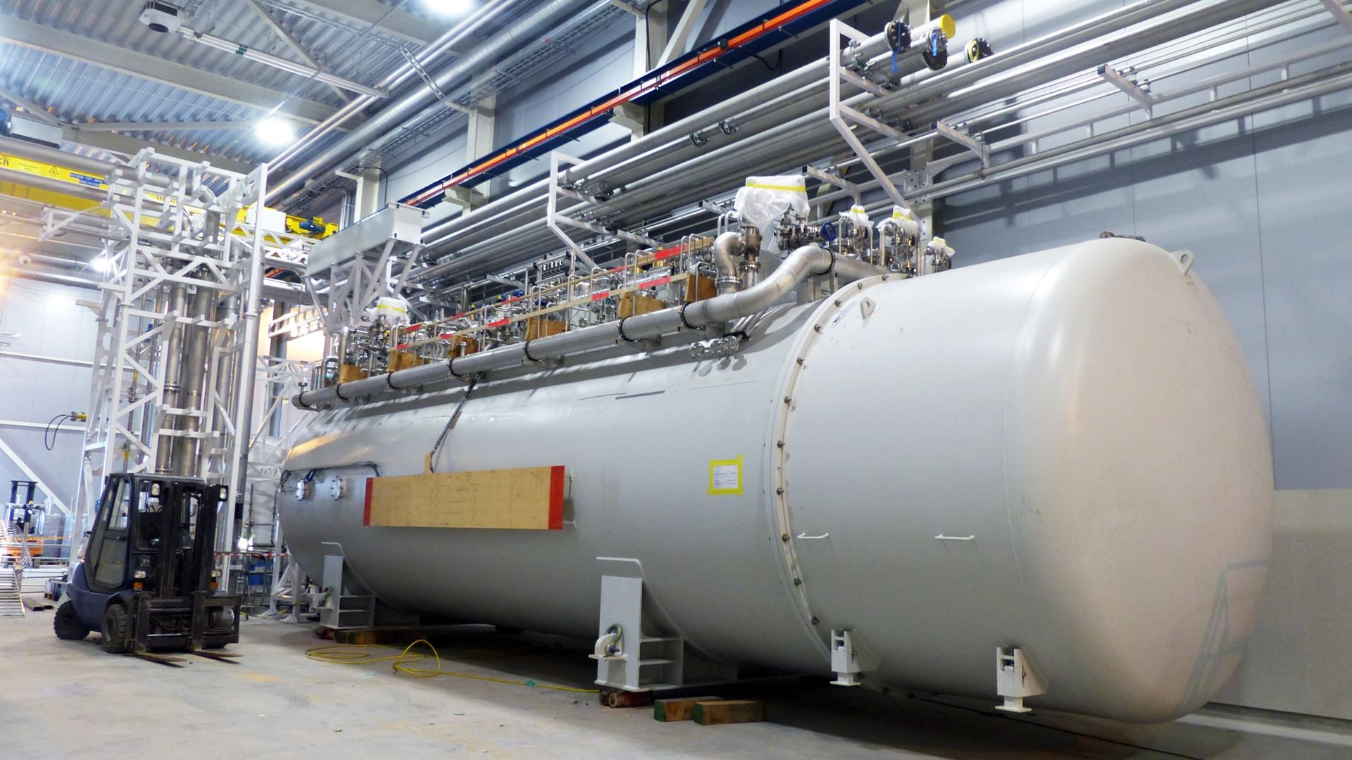 Large industrial pressure vessel with complex piping and fittings inside a spacious warehouse.