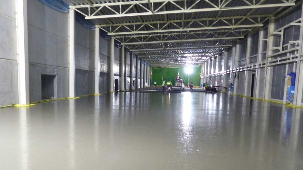 Smooth concrete floor in a large, industrial warehouse with overhead beams and bright lighting.