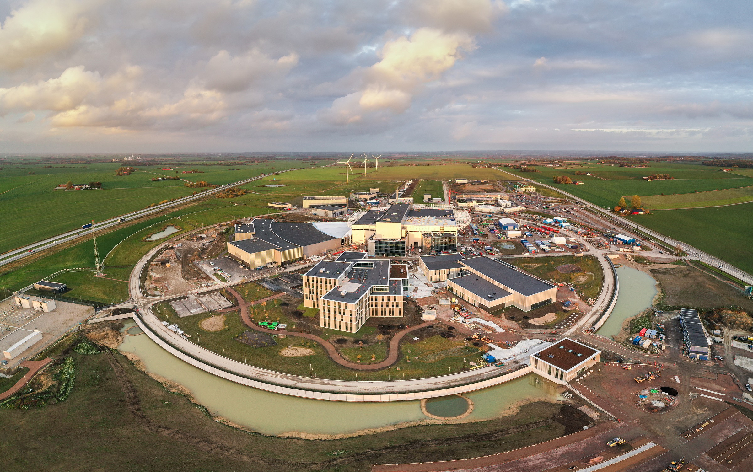 Aerial view of a modern construction site surrounded by green fields and a winding waterway.