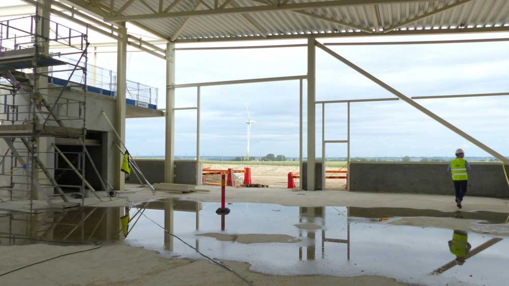 Construction site with scaffolding, large open walls, and a visible wind turbine outside.