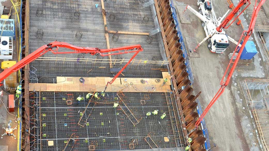 Aerial view of a construction site with workers, cranes, and concrete reinforcement structures.
